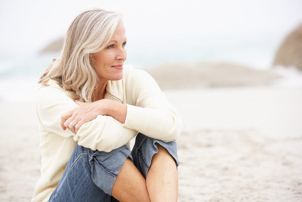 Senior Woman On Holiday Sitting On Winter Beach